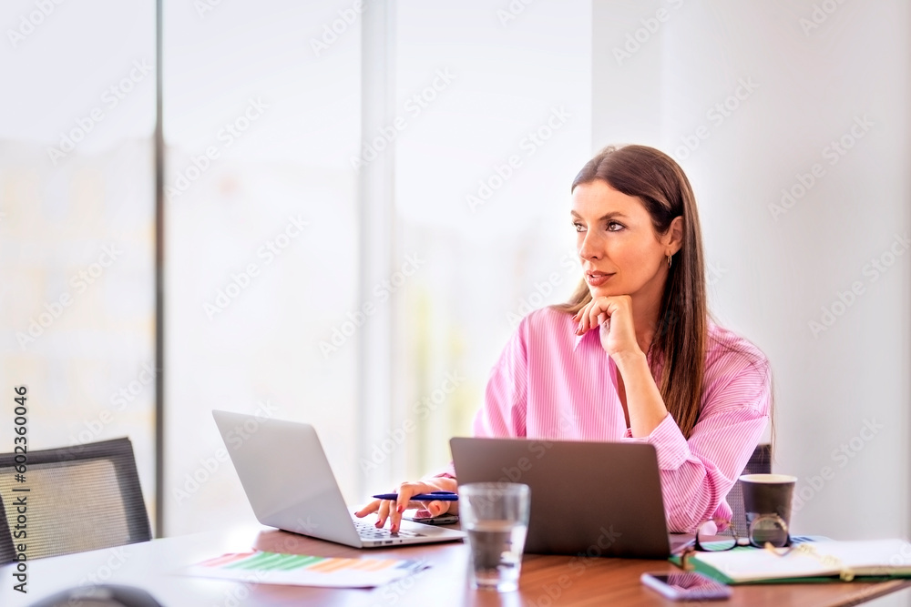 Confindent businesswoman looking thoughtfully and using notebooks in a modern office Confindent businesswoman looking thoughtfully and using notebooks in a modern office