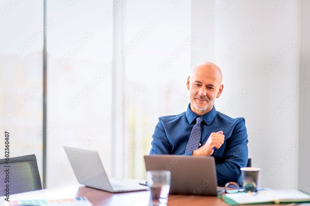 Confident businessman sitting at office desk and using laptops for work Confident businessman sitting at office desk and using laptops for work