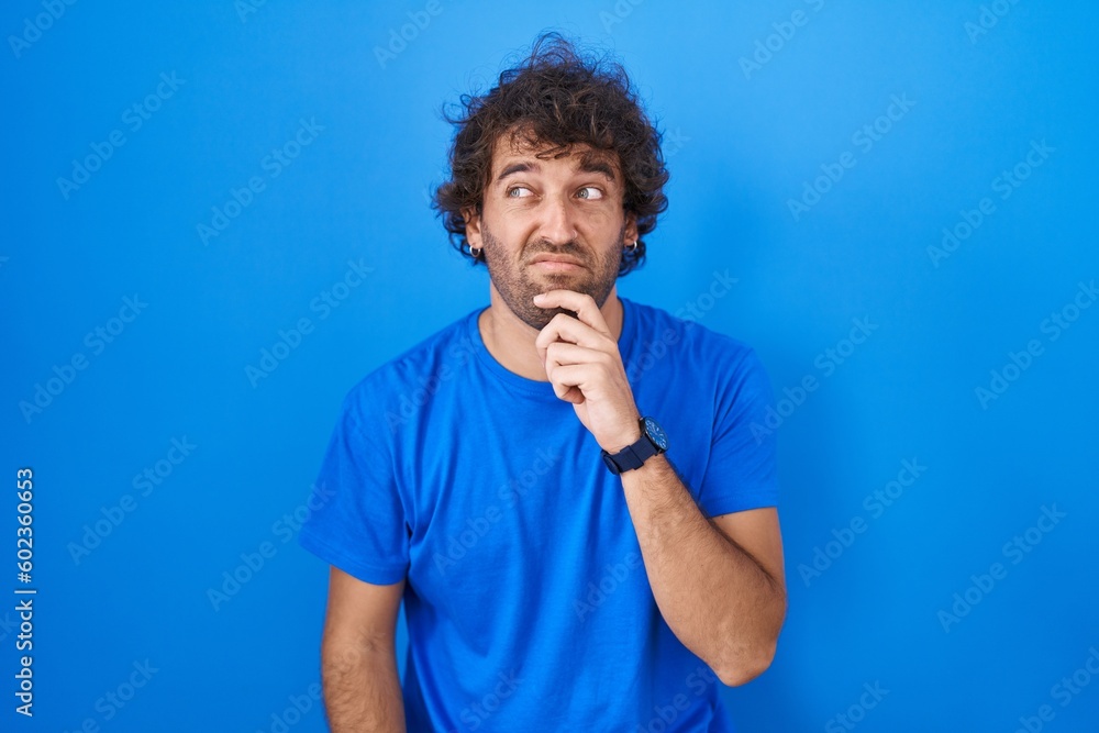 Hispanic young man standing over blue background thinking worried about a question, concerned and nervous with hand on chin Hispanic young man standing over blue background thinking worried about a question, concerned and nervous with hand on chin
