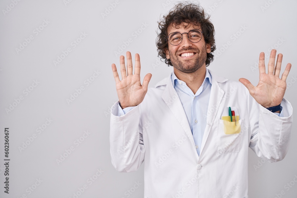 Hispanic young man wearing doctor uniform showing and pointing up with fingers number ten while smiling confident and happy. Hispanic young man wearing doctor uniform showing and pointing up with fingers number ten while smiling confident and happy.