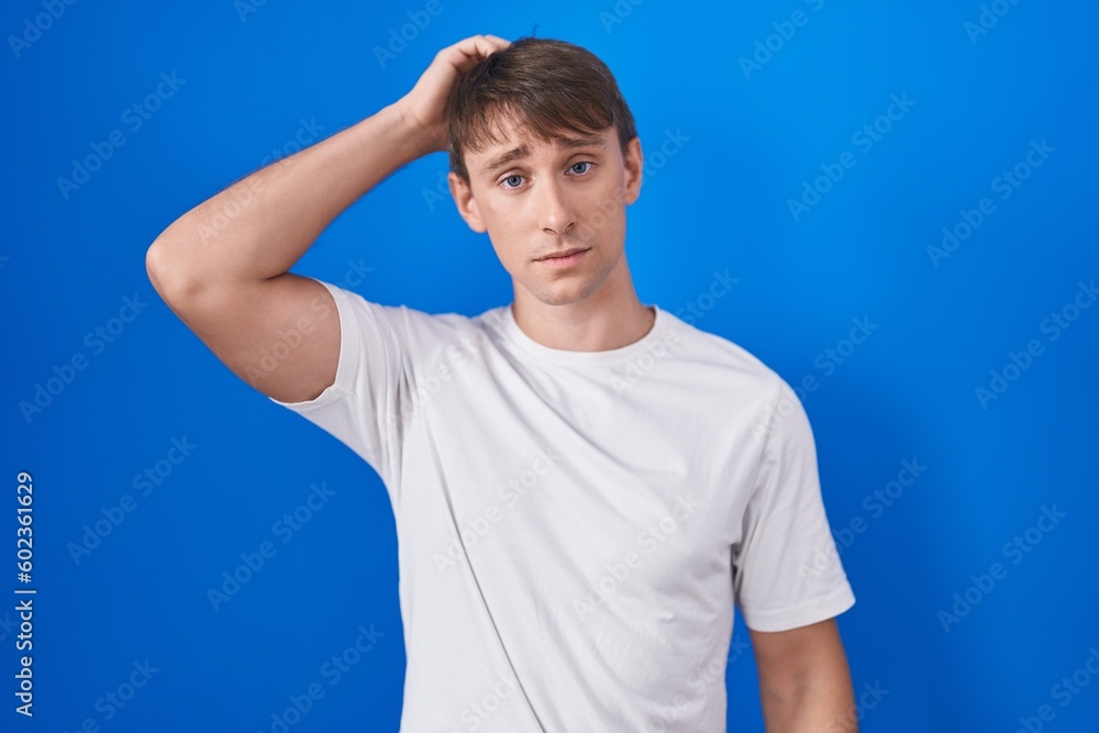 Caucasian blond man standing over blue background confuse and wondering about question. uncertain with doubt, thinking with hand on head. pensive concept. Caucasian blond man standing over blue background confuse and wondering about question. uncertain with doubt, thinking with hand on head. pensive concept.