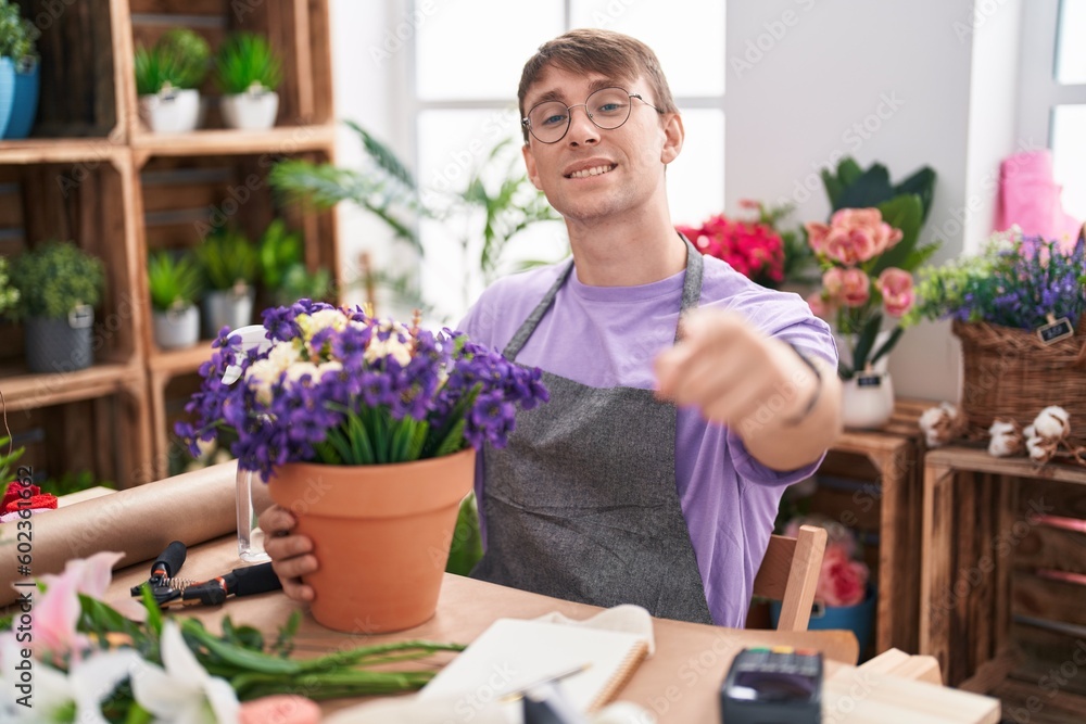 Caucasian blond man working at florist shop pointing to you and the camera with fingers, smiling positive and cheerful