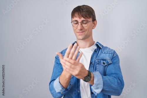 Caucasian blond man standing wearing glasses suffering pain on hands and fingers, arthritis inflammation