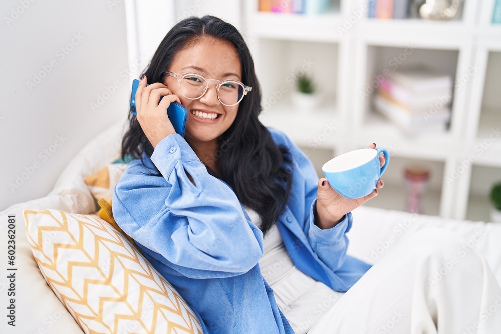 Young chinese woman talking on smartphone drinking coffee at bedroom Young chinese woman talking on smartphone drinking coffee at bedroom