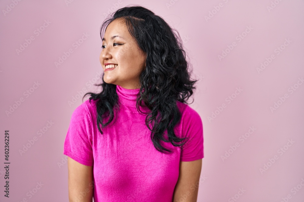 Young asian woman standing over pink background looking away to side with smile on face, natural expression. laughing confident. Young asian woman standing over pink background looking away to side with smile on face, natural expression. laughing confident.