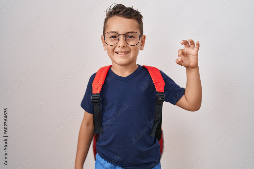 Little hispanic boy wearing glasses and student backpack doing ok sign with fingers, smiling friendly gesturing excellent symbol Little hispanic boy wearing glasses and student backpack doing ok sign with fingers, smiling friendly gesturing excellent symbol