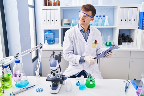 Young man scientist smiling confident reading report at laboratory