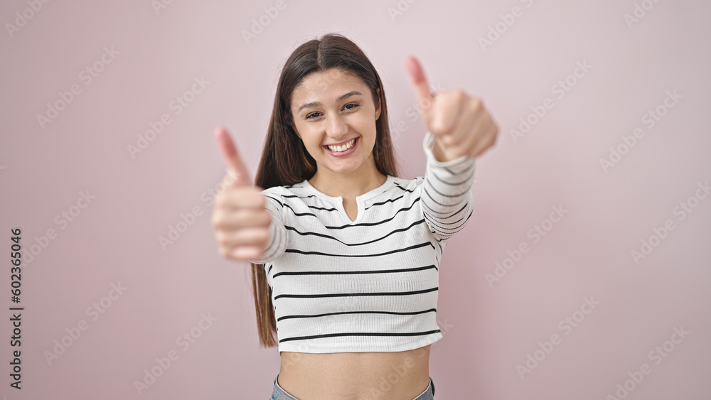 Young beautiful hispanic woman smiling with thumbs up over isolated pink background Young beautiful hispanic woman smiling with thumbs up over isolated pink background