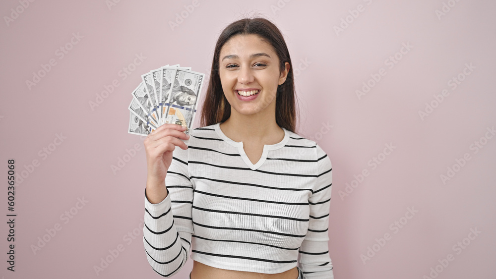 Young beautiful hispanic woman smiling confident holding dollars over isolated pink background Young beautiful hispanic woman smiling confident holding dollars over isolated pink background
