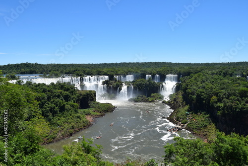 View of the Iguazu Falls hidden among the trees. Boats with tourists sail under the waterfall.