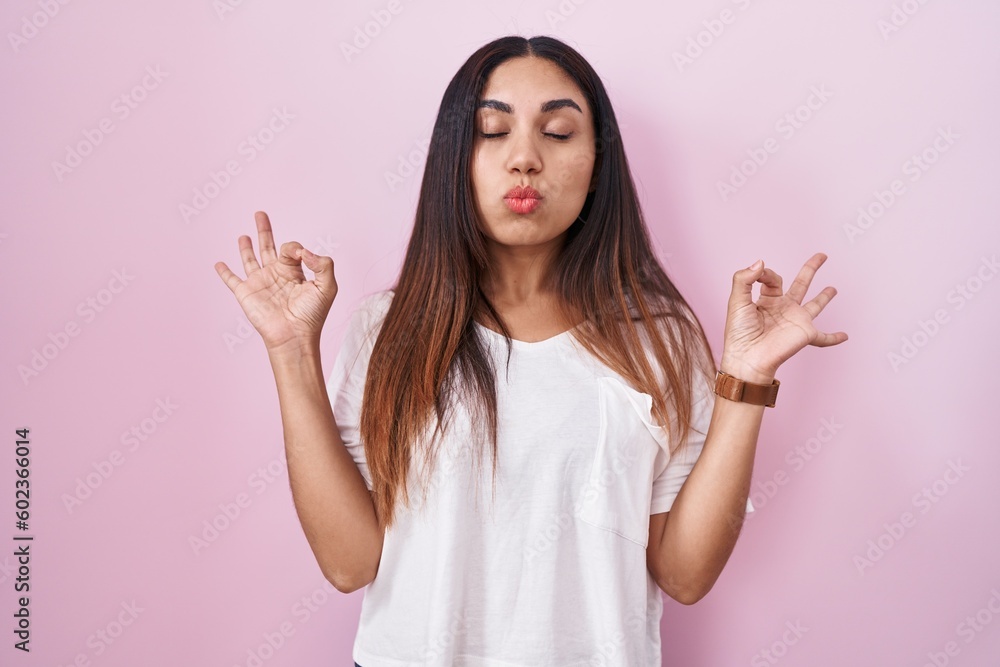 Young arab woman standing over pink background relaxed and smiling with eyes closed doing meditation gesture with fingers. yoga concept. Young arab woman standing over pink background relaxed and smiling with eyes closed doing meditation gesture with fingers. yoga concept.