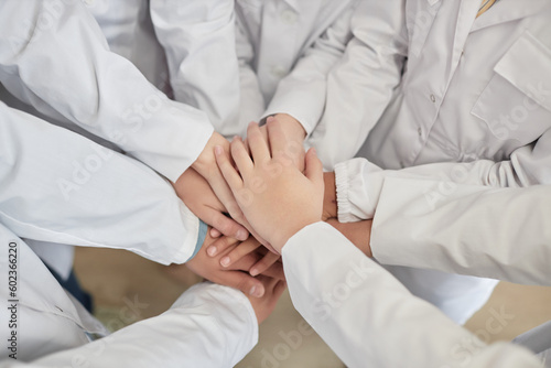 Top view closeup of group of children stacking hands in science class with white lab coats