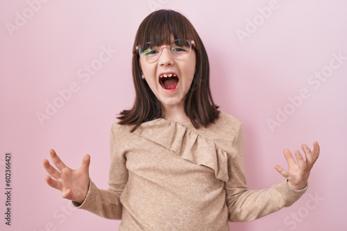Little hispanic girl wearing glasses crazy and mad shouting and yelling with aggressive expression and arms raised. frustration concept.