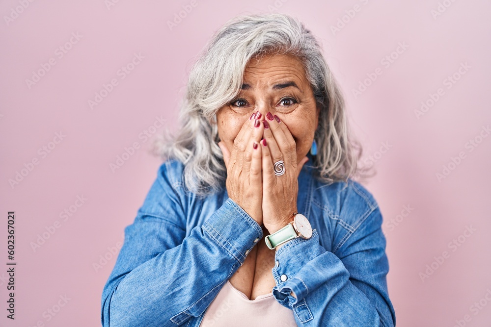 Middle age woman with grey hair standing over pink background laughing and embarrassed giggle covering mouth with hands, gossip and scandal concept Middle age woman with grey hair standing over pink background laughing and embarrassed giggle covering mouth with hands, gossip and scandal concept