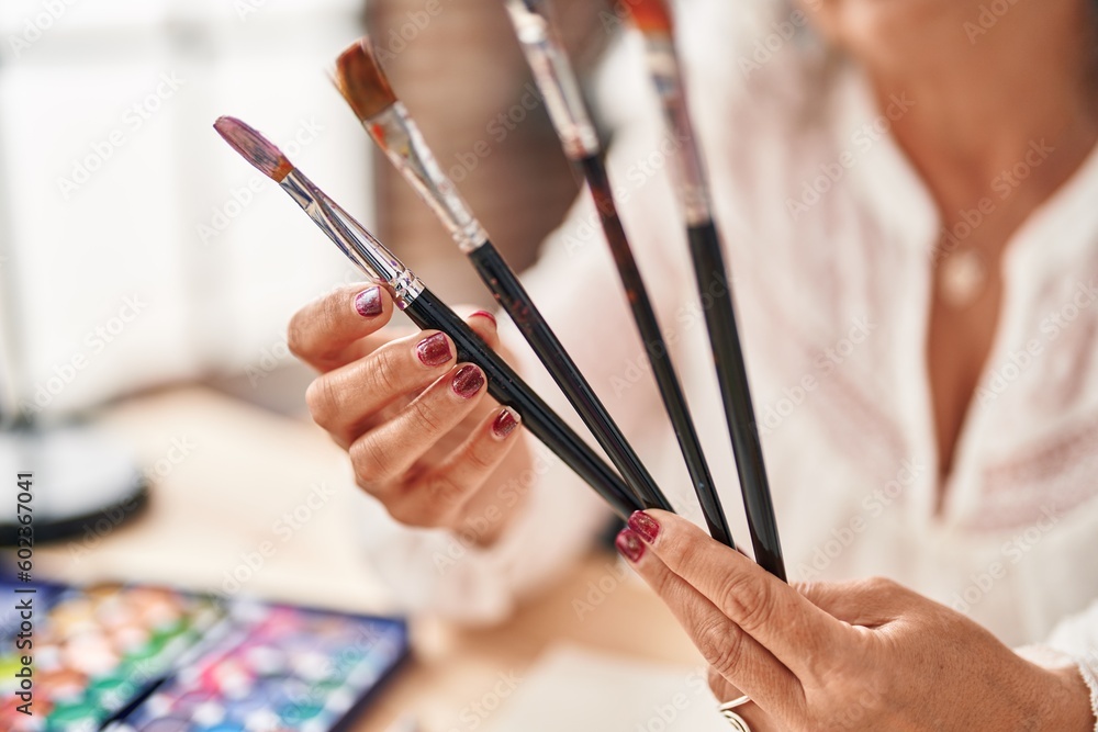 Middle age woman artist holding paintbrushes at art studio Middle age woman artist holding paintbrushes at art studio
