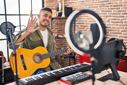 Young hispanic man doing online guitar tutorial looking positive and happy standing and smiling with a confident smile showing teeth