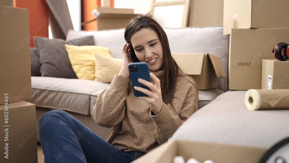 Beautiful hispanic woman using smartphone sitting on floor at new home Beautiful hispanic woman using smartphone sitting on floor at new home