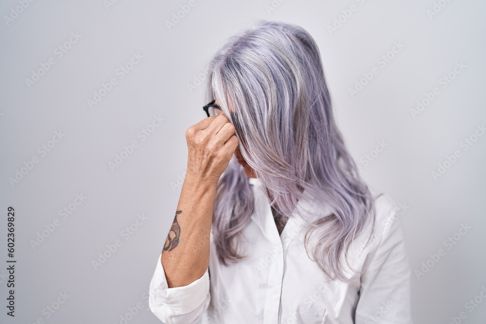 Middle age woman with tattoos wearing glasses standing over white background tired rubbing nose and eyes feeling fatigue and headache. stress and frustration concept. Middle age woman with tattoos wearing glasses standing over white background tired rubbing nose and eyes feeling fatigue and headache. stress and frustration concept.
