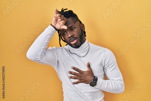 African man with dreadlocks wearing turtleneck sweater over yellow background touching forehead for illness and fever, flu and cold, virus sick