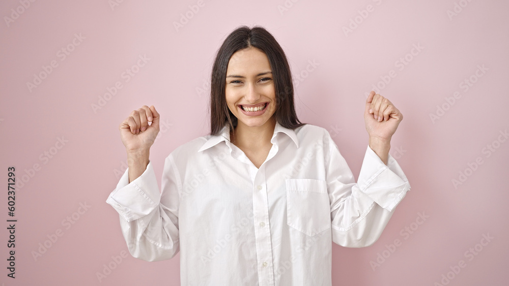 Young beautiful hispanic woman smiling confident standing with fists raised up over isolated pink background Young beautiful hispanic woman smiling confident standing with fists raised up over isolated pink background