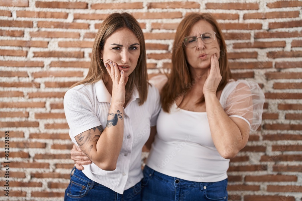 Hispanic mother and daughter wearing casual white t shirt touching mouth with hand with painful expression because of toothache or dental illness on teeth. dentist concept. Hispanic mother and daughter wearing casual white t shirt touching mouth with hand with painful expression because of toothache or dental illness on teeth. dentist concept.