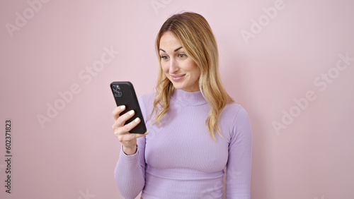 Young beautiful hispanic woman using smartphone with surprise expression over isolated pink background