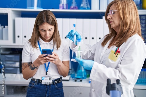 Mother and daughter scientists using smartphone holding test tubes at laboratory