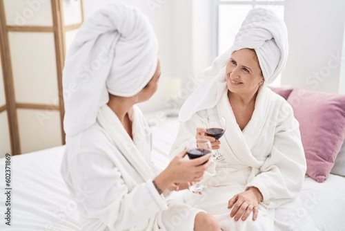 Mother and daughter wearing bathrobe drinking glass of wine at bedroom © Krakenimages.com