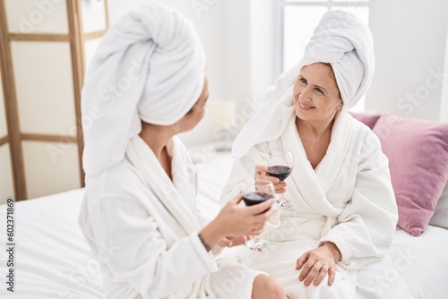 Mother and daughter wearing bathrobe drinking glass of wine at bedroom