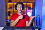 Young hispanic man playing video games amazed and smiling to the camera while presenting with hand and pointing with finger.