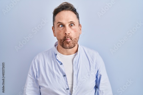 Middle age caucasian man standing over blue background making fish face with lips, crazy and comical gesture. funny expression.