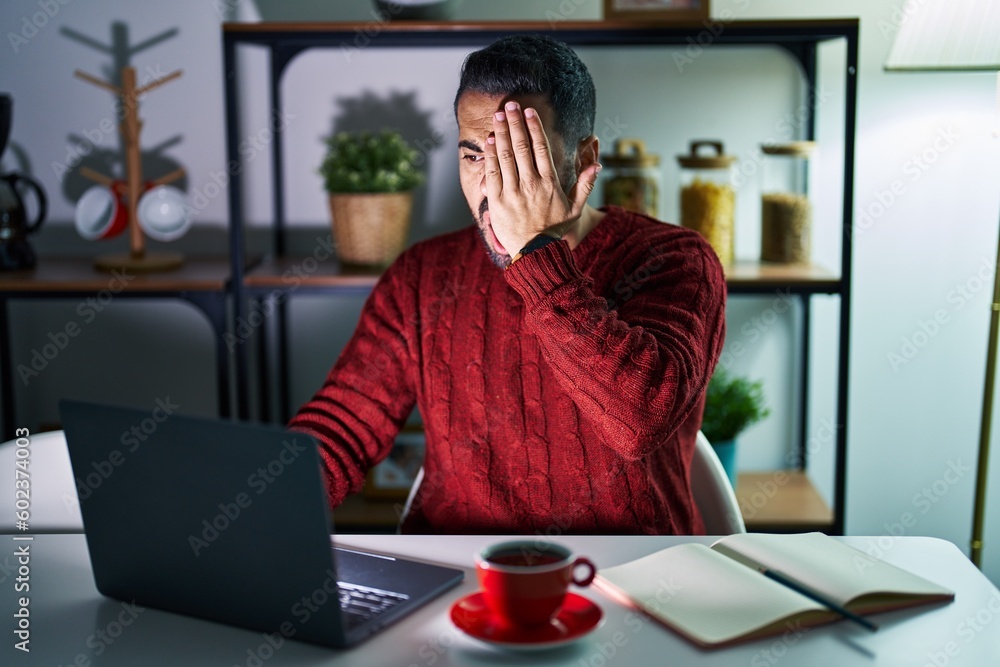 Young hispanic man with beard using computer laptop at night at home yawning tired covering half face, eye and mouth with hand. face hurts in pain. Young hispanic man with beard using computer laptop at night at home yawning tired covering half face, eye and mouth with hand. face hurts in pain.