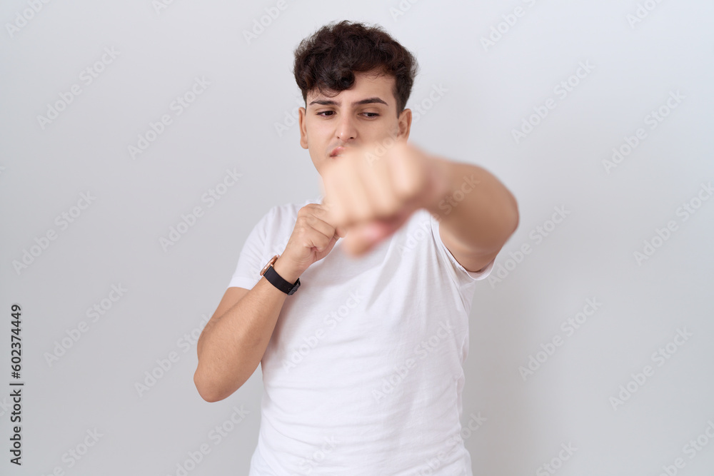 Young non binary man wearing casual white t shirt punching fist to fight, aggressive and angry attack, threat and violence Young non binary man wearing casual white t shirt punching fist to fight, aggressive and angry attack, threat and violence