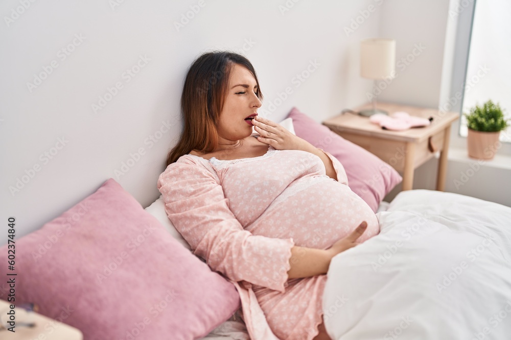 Young pregnant woman yawning sitting on bed at bedroom Young pregnant woman yawning sitting on bed at bedroom
