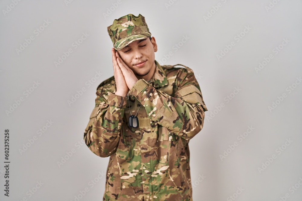 Young arab man wearing camouflage army uniform sleeping tired dreaming and posing with hands together while smiling with closed eyes. Young arab man wearing camouflage army uniform sleeping tired dreaming and posing with hands together while smiling with closed eyes.