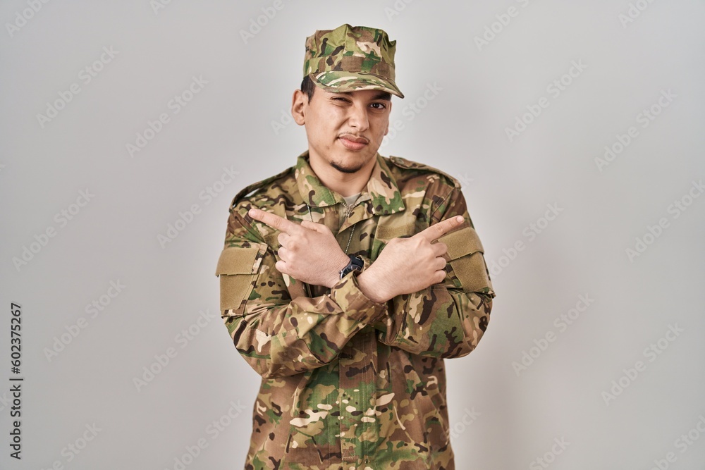 Young arab man wearing camouflage army uniform pointing to both sides with fingers, different direction disagree Young arab man wearing camouflage army uniform pointing to both sides with fingers, different direction disagree