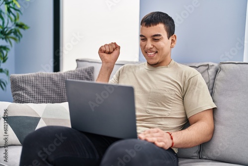 Young arab man using laptop at home screaming proud, celebrating victory and success very excited with raised arm © Krakenimages.com