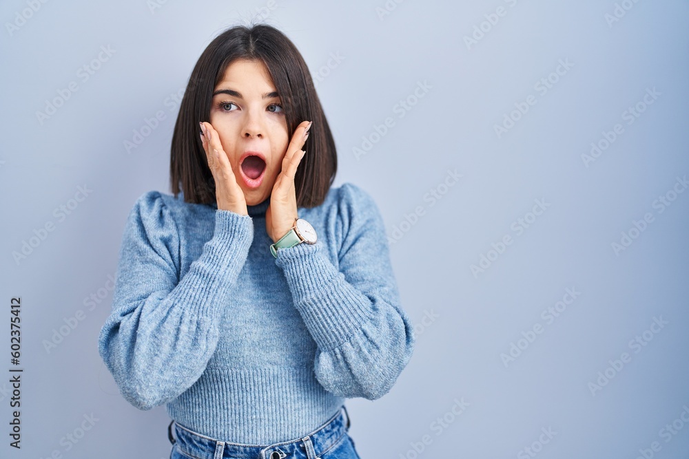 Young hispanic woman standing over blue background afraid and shocked, surprise and amazed expression with hands on face Young hispanic woman standing over blue background afraid and shocked, surprise and amazed expression with hands on face