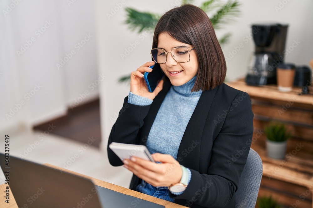 Young beautiful hispanic woman business worker talking on smartphone reading notebook at office Young beautiful hispanic woman business worker talking on smartphone reading notebook at office