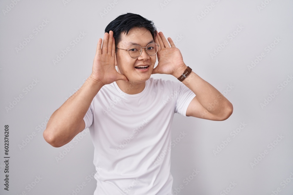 Young asian man standing over white background smiling cheerful playing peek a boo with hands showing face. surprised and exited Young asian man standing over white background smiling cheerful playing peek a boo with hands showing face. surprised and exited