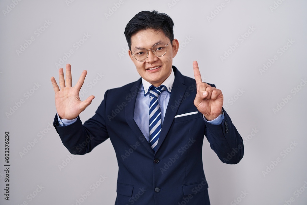 Young asian man wearing business suit and tie showing and pointing up with fingers number six while smiling confident and happy. Young asian man wearing business suit and tie showing and pointing up with fingers number six while smiling confident and happy.