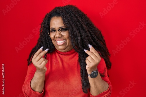 Plus size hispanic woman standing over red background doing money gesture with hands, asking for salary payment, millionaire business © Krakenimages.com