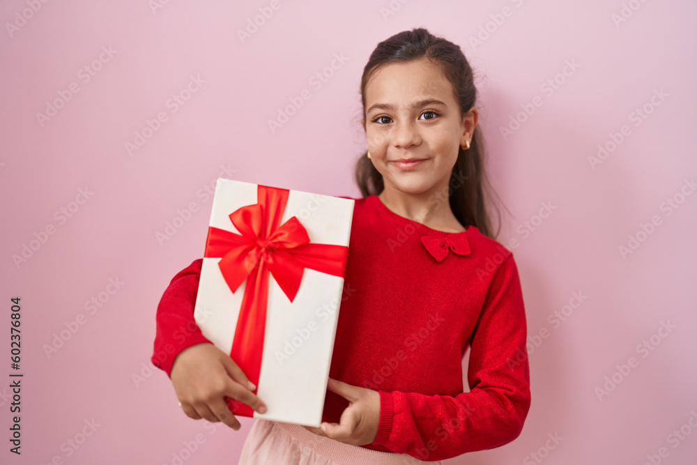 Fototapeta premium Little hispanic girl holding a gifts looking positive and happy standing and smiling with a confident smile showing teeth