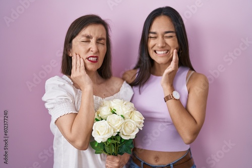 Hispanic mother and daughter holding bouquet of white flowers touching mouth with hand with painful expression because of toothache or dental illness on teeth. dentist concept.