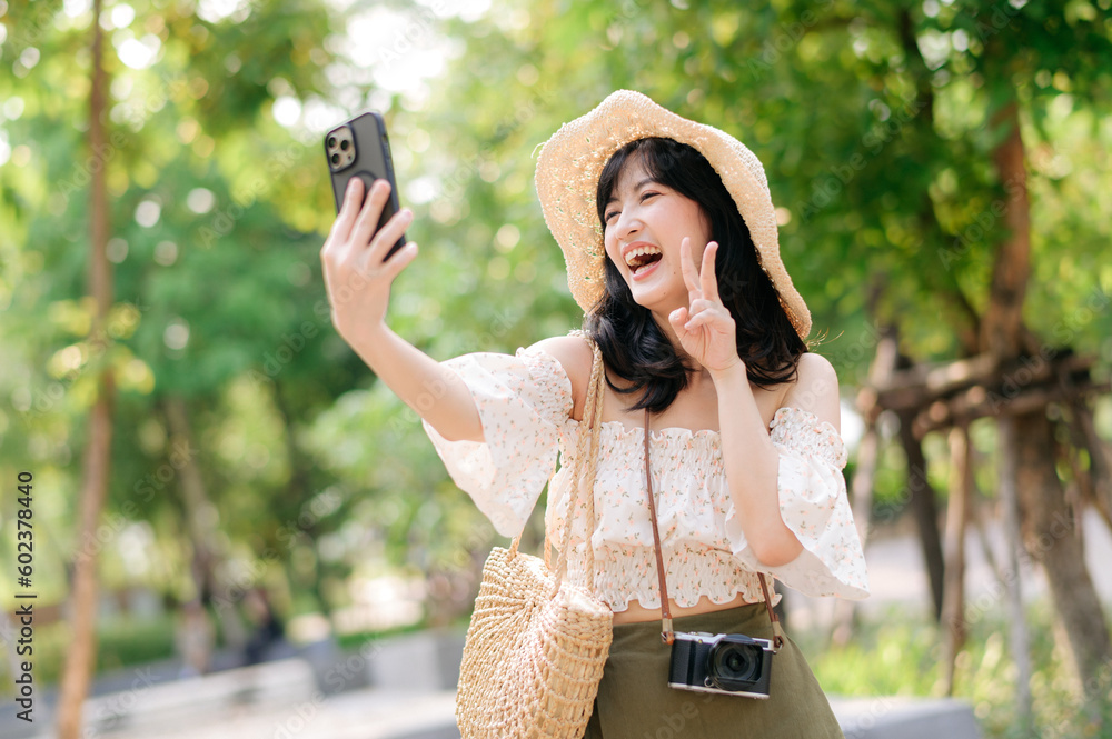 Portrait of asian young woman traveler with weaving hat, basket, mobile phone and camera on green public park background. Journey trip lifestyle, world travel explorer or Asia summer tourism concept.