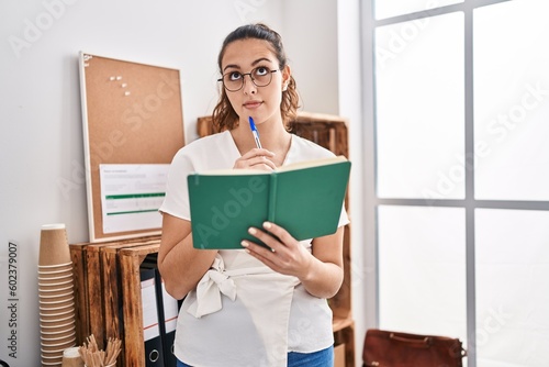 Young beautiful hispanic woman business worker reading book with doubt expression at office photo