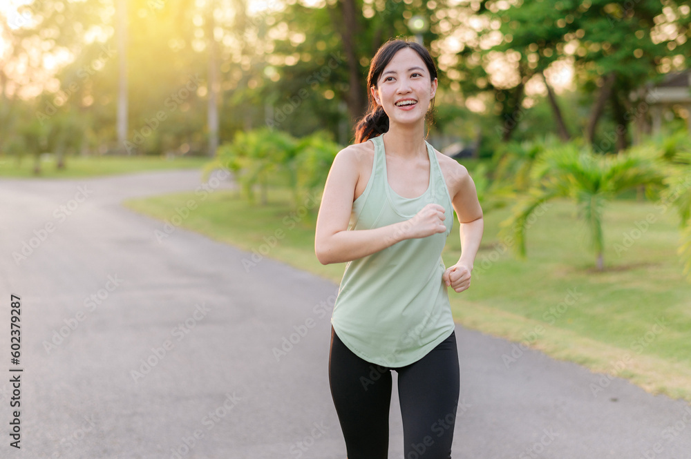 Fit Asian young woman jogging in park smiling happy running and enjoying a healthy outdoor lifestyle. Female jogger. Fitness runner girl in public park. healthy lifestyle and wellness being concept Fit Asian young woman jogging in park smiling happy running and enjoying a healthy outdoor lifestyle. Female jogger. Fitness runner girl in public park. healthy lifestyle and wellness being concept