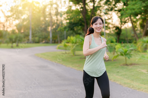 Fit Asian young woman jogging in park smiling happy running and enjoying a healthy outdoor lifestyle. Female jogger. Fitness runner girl in public park. healthy lifestyle and wellness being concept