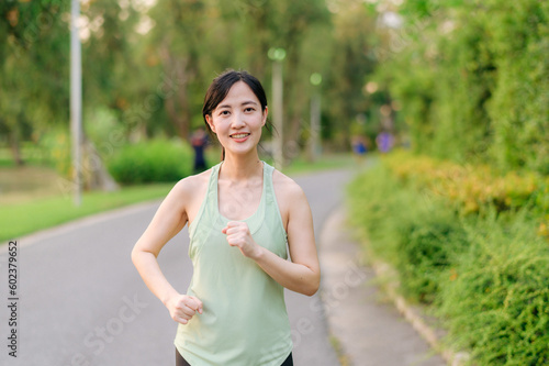 Fit Asian young woman jogging in park smiling happy running and enjoying a healthy outdoor lifestyle. Female jogger. Fitness runner girl in public park. healthy lifestyle and wellness being concept