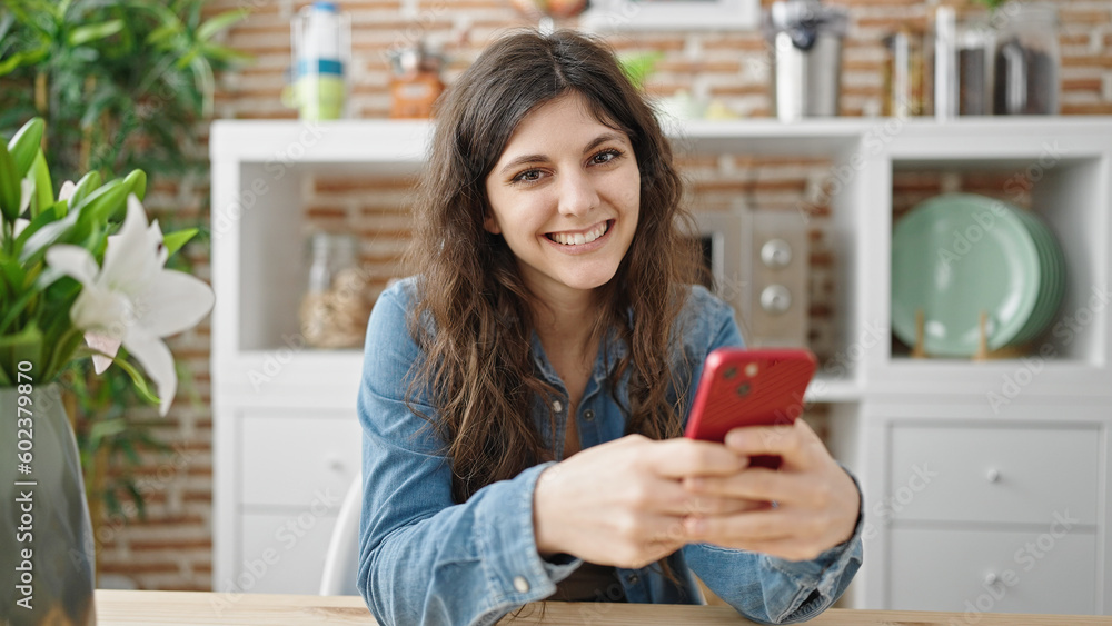 Young beautiful hispanic woman using smartphone sitting on table at dinning room Young beautiful hispanic woman using smartphone sitting on table at dinning room